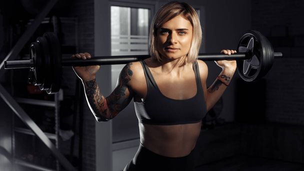 Young sporty blonde woman doing heavy barbell exercise in fitness class. - Photo, Image