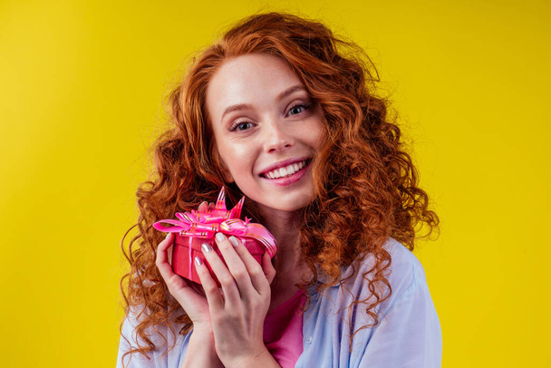 redhair curly ginger woman holding gift box in studio yellow background.mothers day and eighth of marchor St. Valentines Day concept - Foto, imagen