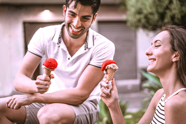 Двое молодых влюбленных едят мороженое, сидя на скамейке под открытым небом. Концепция отдыха
 - Фото, изображение