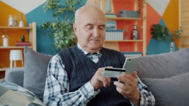 Retired man shopping online making payment with bank card and smartphone - Video, Çekim