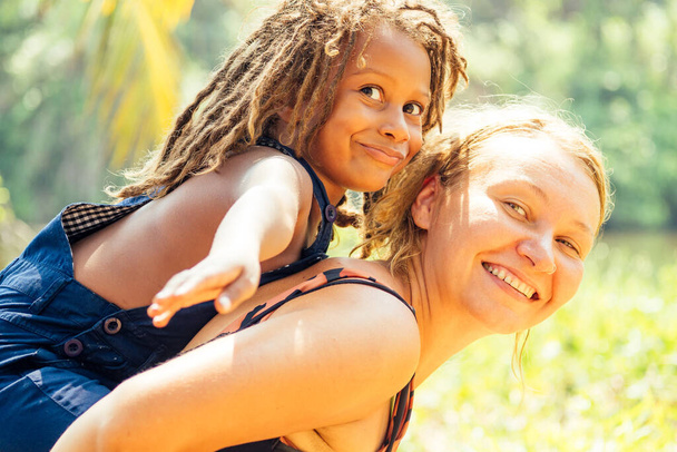 Mowgli indian boy with dreadlocks hair and caucasian mother hugging in tropics green forest background.adoption concept - Фото, зображення