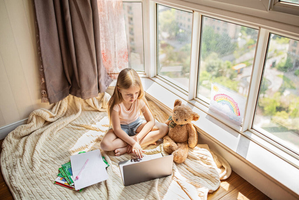 Pretty schoolgirl studying homework during her online lesson at home, social distance during quarantine covid-19, self-isolation, online education concept, home schooler. Workplace in living room - Foto, imagen