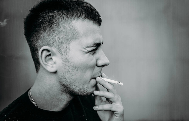 Portrait of a young man smoking a cigarette near a building wall - Photo, image