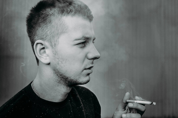 Portrait of a young man smoking a cigarette near a building wall - Фото, изображение
