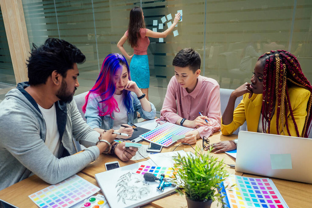 creative agency designer team working together:african american woman with dreadlocks pigtails and caucasian girl pink blue multi-colored hair communication with indian man in office - Foto, Bild