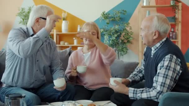 Joyful pensioners talking laughing doing high-five during tea party in apartment - Materiaali, video