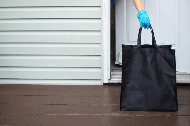 Una persona che indossa i guanti, che prende una borsa della spesa da un'entrata di casa
 - Foto, immagini