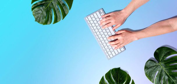 Person using a computer keyboard with tropical leaves - Photo, Image