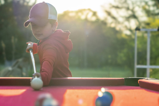 Ένα μικρό αγόρι παίζει μπιλιάρδο σε ένα υπαίθριο περιβάλλον - Φωτογραφία, εικόνα