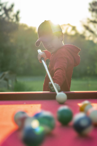 A small young boy plays pool in an outdoor environment - Photo, Image