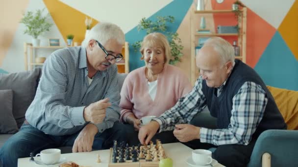 Happy retired men playing chess game while cheerful woman watching and smiling - Filmati, video