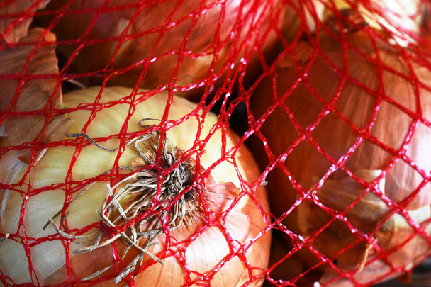 A close up image of several white onions in a red mesh bag for freshness.  - Photo, Image