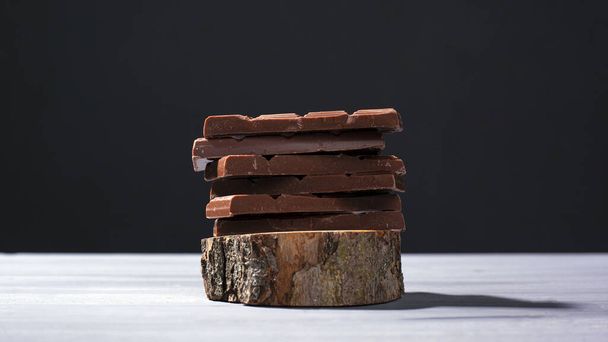 pieces of milk chocolate on a wooden stand on a gray background - Photo, Image