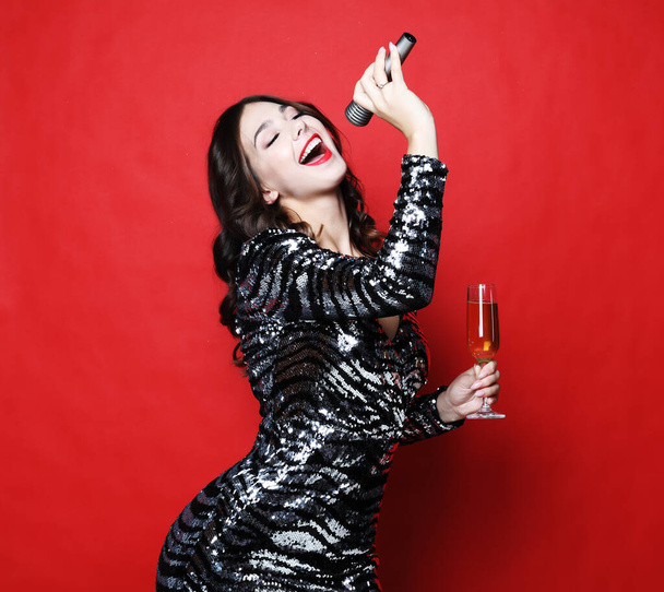 Young woman in black evening dress holding glass of champagne and microphone. - Photo, Image