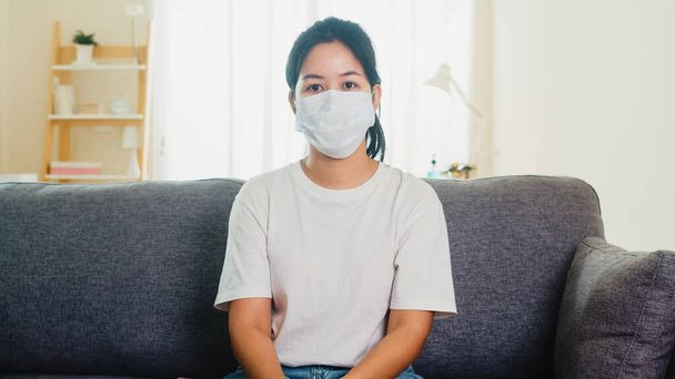 Depressieve Aziatische zakenvrouw met beschermende masker zittend op de bank in de woonkamer thuis wanneer sociale afstand verblijf thuis en self quarantaine tijd, pandemie in China, coronavirus concept. - Foto, afbeelding