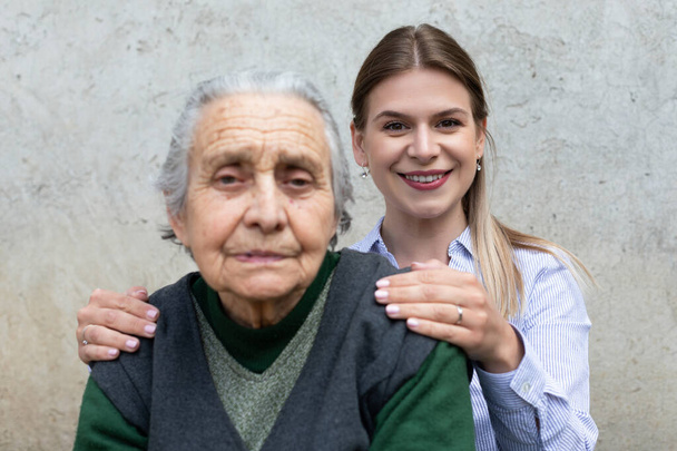 Junge freundliche Frau umarmt Seniorin im Freien - gemeinsam verbrachte Zeit - Foto, Bild