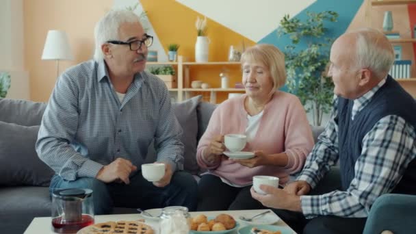 Old people friends talking drinking tea doing high-five sitting at table with food - Materiaali, video
