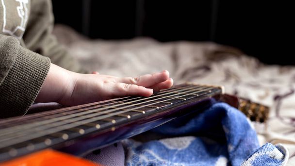 mano dei bambini sul collo di un colore arancione chitarra acustica. imparare a suonare lo strumento
 - Foto, immagini