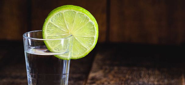 high quality distilled alcohol. Brazilian cachaca (called pinga) taken with lemon, drip, vodka, white rum, spirits, ozo, sake or brandy. Drink on rustic wooden background. - Photo, Image