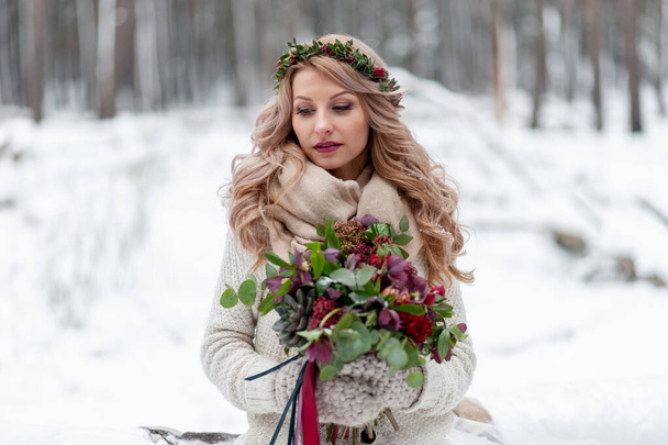 Молода дівчина слов'янського вигляду з вінок польових квітів. Прекрасна блондинка тримає букет на зимовому фоні.. - Фото, зображення