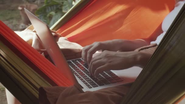 Bezimienna kobieta ręce wpisując notatnik klawiatury na zewnątrz na tle natury letniej. Nierozpoznana kobieta freelancer pracuje na laptopie w hamaku w zwolnionym tempie. Praca na zlecenie telepraca daleko - Materiał filmowy, wideo