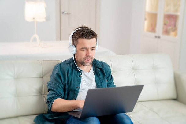 freelancer listens audio headphones sit on sofa - Фото, изображение