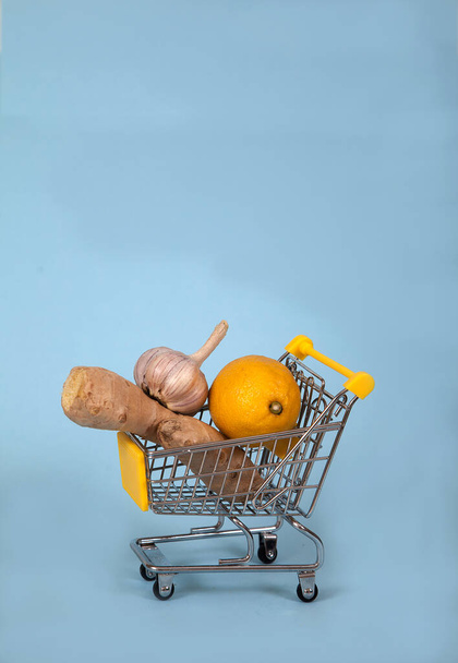 Ginger and lemon and garlic lie inside the supermarket trolley on a blue background. Healthy foods. Health. covyd 19. copy spaes. - Photo, image