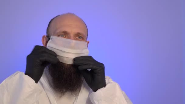 Bearded Caucasian man in a white protective suit and black gloves wearing a mask, goggles and hood. - Кадры, видео