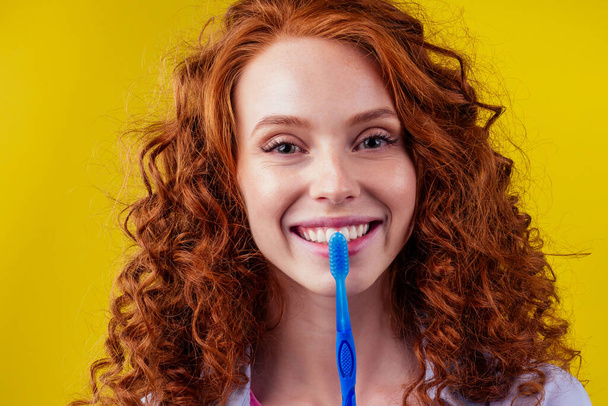 redhaired ginger woman brushing teeth with toothpaste eco paste on yellow studio background - Valokuva, kuva