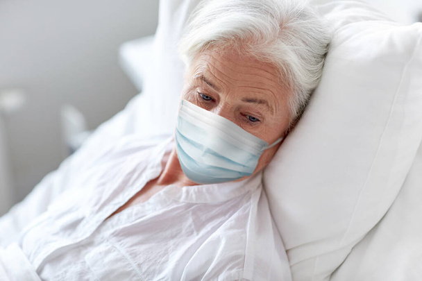 old woman patient in mask lying in bed at hospital - Фото, изображение