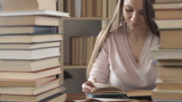 girl is sitting at table in library among many books and textbooks. student reads books and turns pages. Exam preparation. The student studies at home. home education. The concept of modern education. - Filmagem, Vídeo
