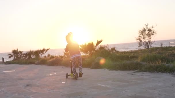 A little girl rides a scooter along the sea in the evening - Footage, Video