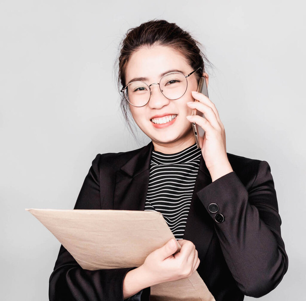 Giovane intelligente bella donna d'affari asiatica indossava abito nero e occhiali, intelligente e pensare tenendo Documento, telefono parlante
 - Foto, immagini