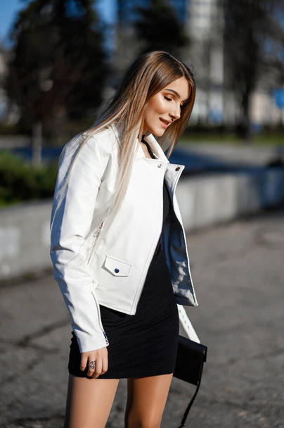 Attractive blonde in a black dress and white leather walks around the city - Zdjęcie, obraz