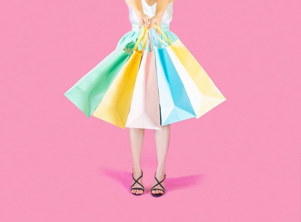 The woman low body part wore blue skirt and black high heels. Carrying a shopping bag in many pastel colors on pink background selective focus - 写真・画像