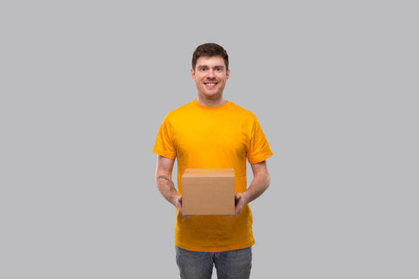 Доставщик с коробкой в руках. Курьер в жёлтой футболке. Доставка на дом. Герой карантина. Isolated
 - Фото, изображение