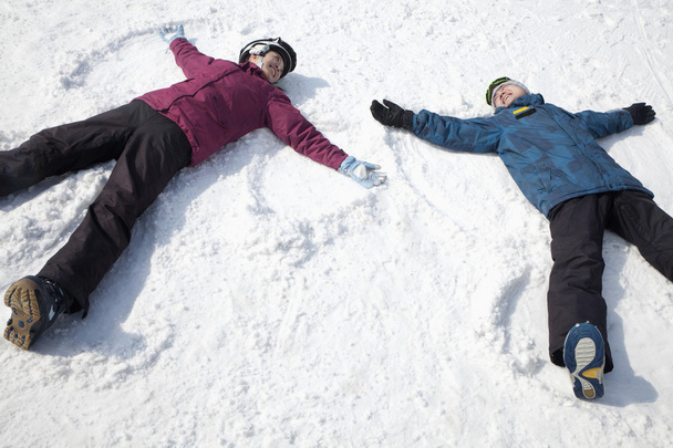 άνδρας και γυναίκα, που βρίσκεται πάνω στο χιόνι που κάνει τον άγγελο χιονιού - Φωτογραφία, εικόνα