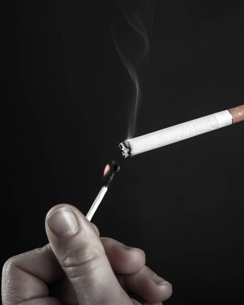 закуривая сигарету горящим спичкой в черно-белом
 - Фото, изображение