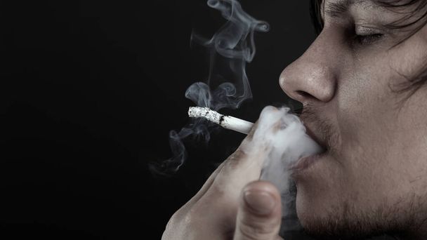 De man rookt een sigaret op donkere achtergrond. depressieve persoon  - Foto, afbeelding