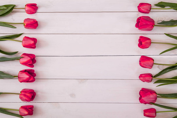Περιγράμματα από φρέσκες ροζ τουλίπες τοποθετημένες στα πλαϊνά του λευκού ρουστίκ ξύλινου φόντου με αντιγραφικό χώρο, πάνω όψη. Άνοιξη λουλούδια για την ημέρα της μητέρας και το Πάσχα - Φωτογραφία, εικόνα