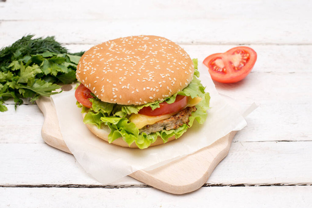 Крупный план свежего домашнего гамбургера лучше на старой белой деревянной доске с помидорами, сыром и красным луком
. - Фото, изображение