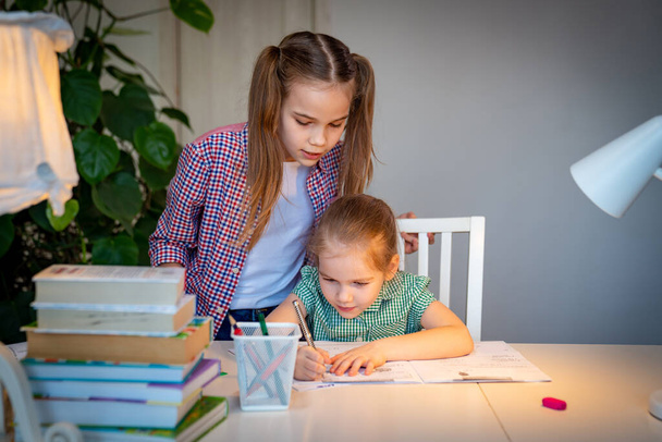 teen sister helps younger with lessons at home. - Φωτογραφία, εικόνα