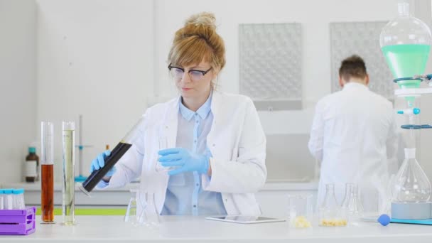 Two scientists working with hemp CBD and CBDa oils and tablet in laboratory. They are using latex gloves, glass tubes and erlenmeyer flasks. Healthcare pharmacy from cannabis seeds. - Materiał filmowy, wideo