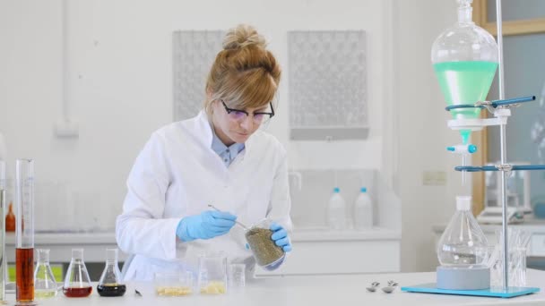 Scientifique chimiste portant des lunettes travaillant avec des huiles de chanvre CBD et CBDa en laboratoire. Elle utilise des gants en latex, des tubes en verre et des flacons d'erlenmeyer. Pharmacie de soins de santé à partir de graines de cannabis. - Séquence, vidéo