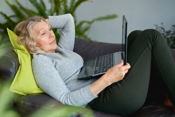 Woman lying on a sofa at home with a laptop - Valokuva, kuva