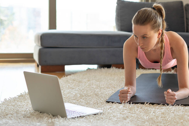 Online sport fitness yoga training. young woman and doing exercises on yoga mat opposite laptop with online master class. training at home - Foto, afbeelding