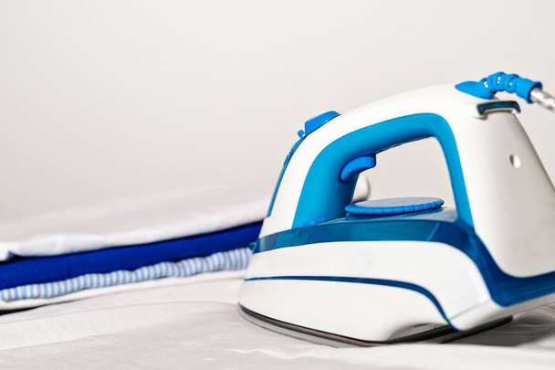 Electric iron and shirt on ironing board. Ironing clothes close up - Zdjęcie, obraz