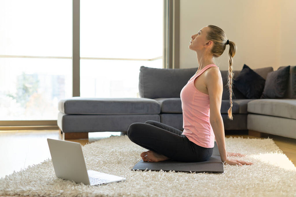 Çevrimiçi spor fitness yoga eğitimi. Genç bir kadın ve yoga minderinde alıştırmalar yapıyor. Bilgisayarın karşısında ana sınıfla birlikte. evde eğitim - Fotoğraf, Görsel