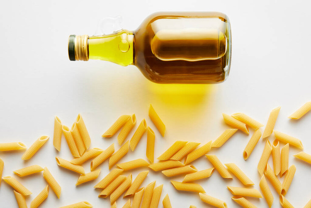 Top view of bottle of olive oil near pasta on white background  - Photo, image