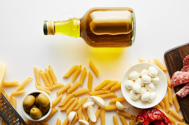 Верхний вид бутылки оливкового масла и макарон с ингредиентами на белом фоне
  - Фото, изображение